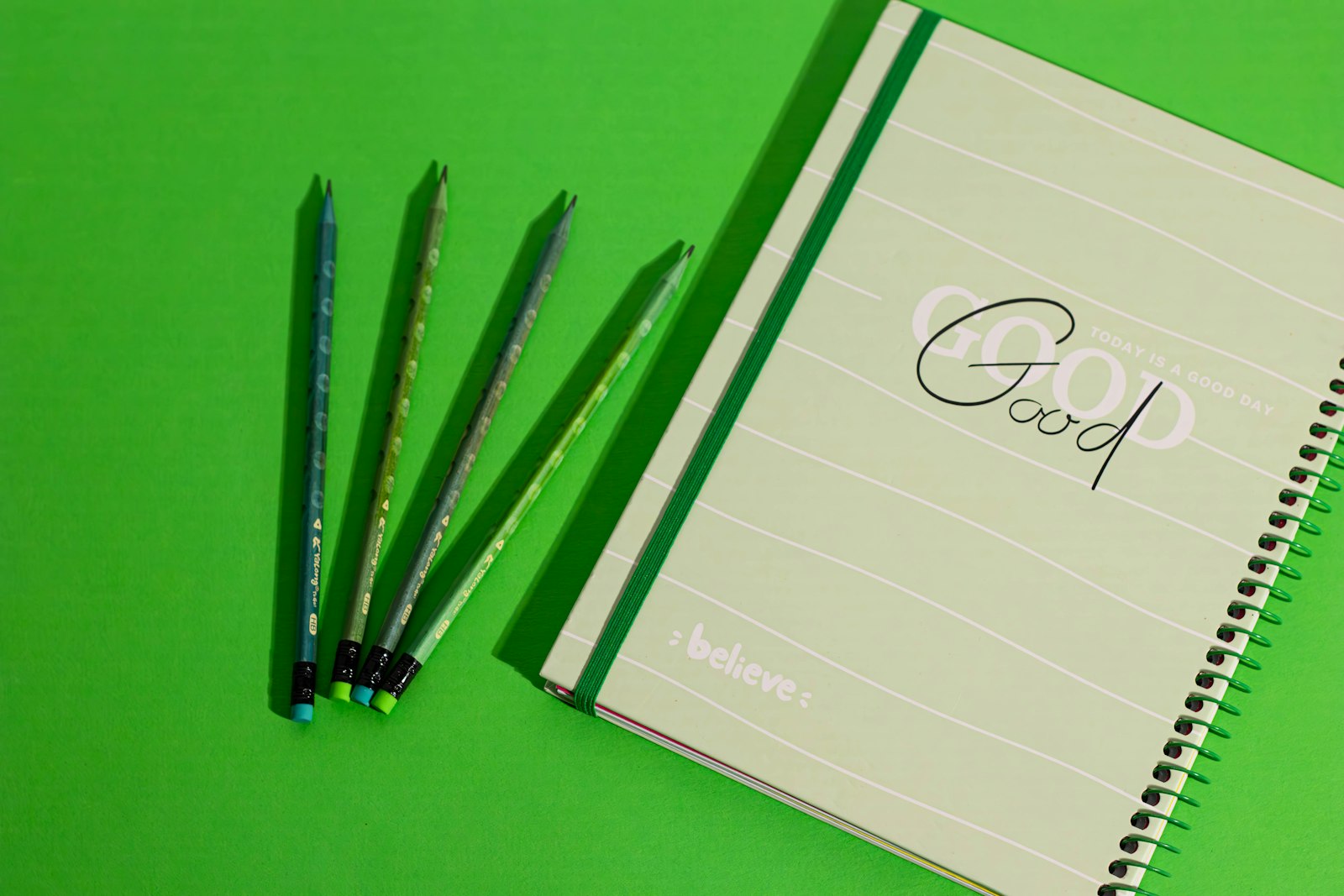 Cuaderno y lápices sobre fondo verde