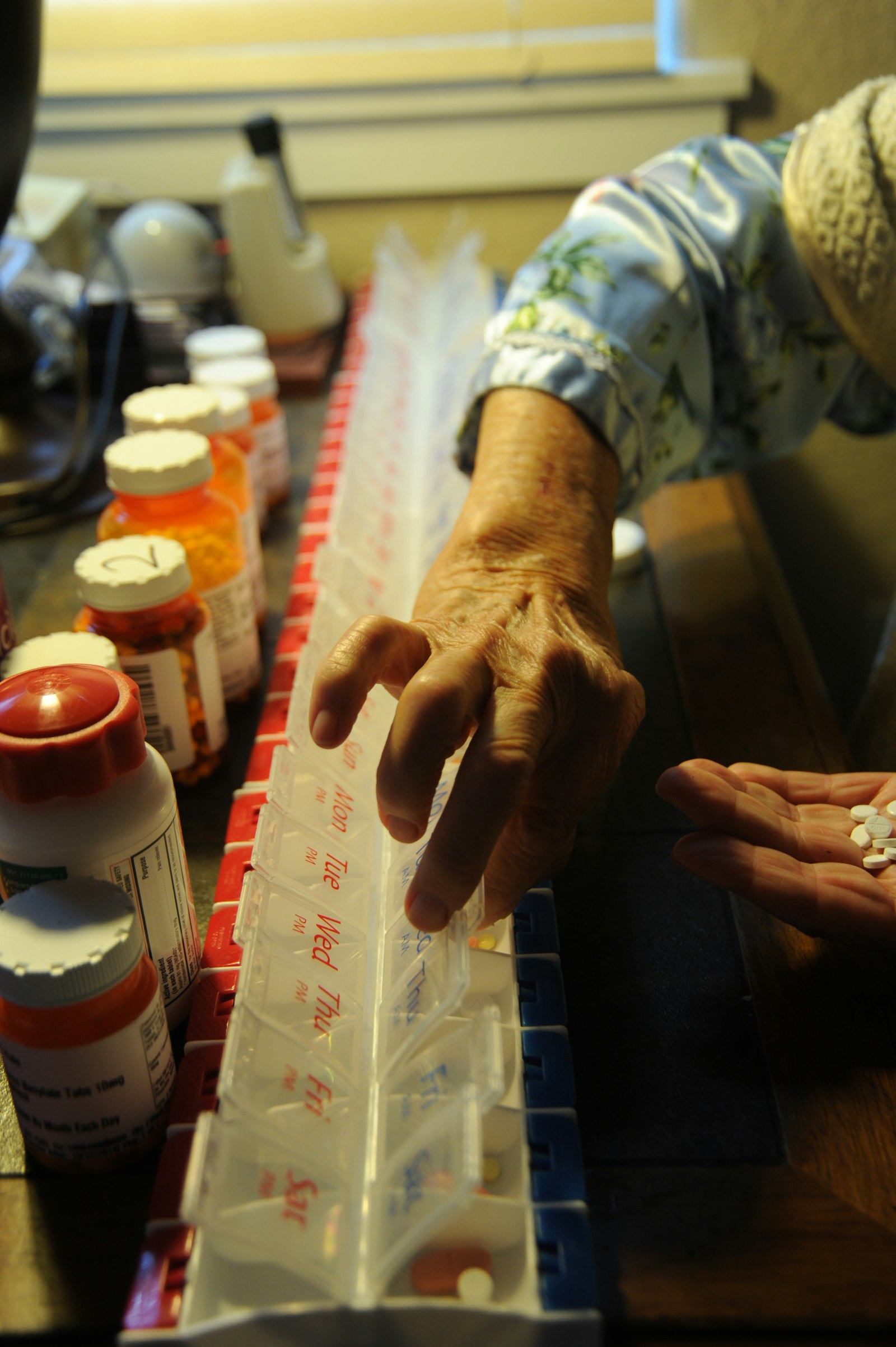 Persona alcanzando un frasco de pastillas sobre la mesa